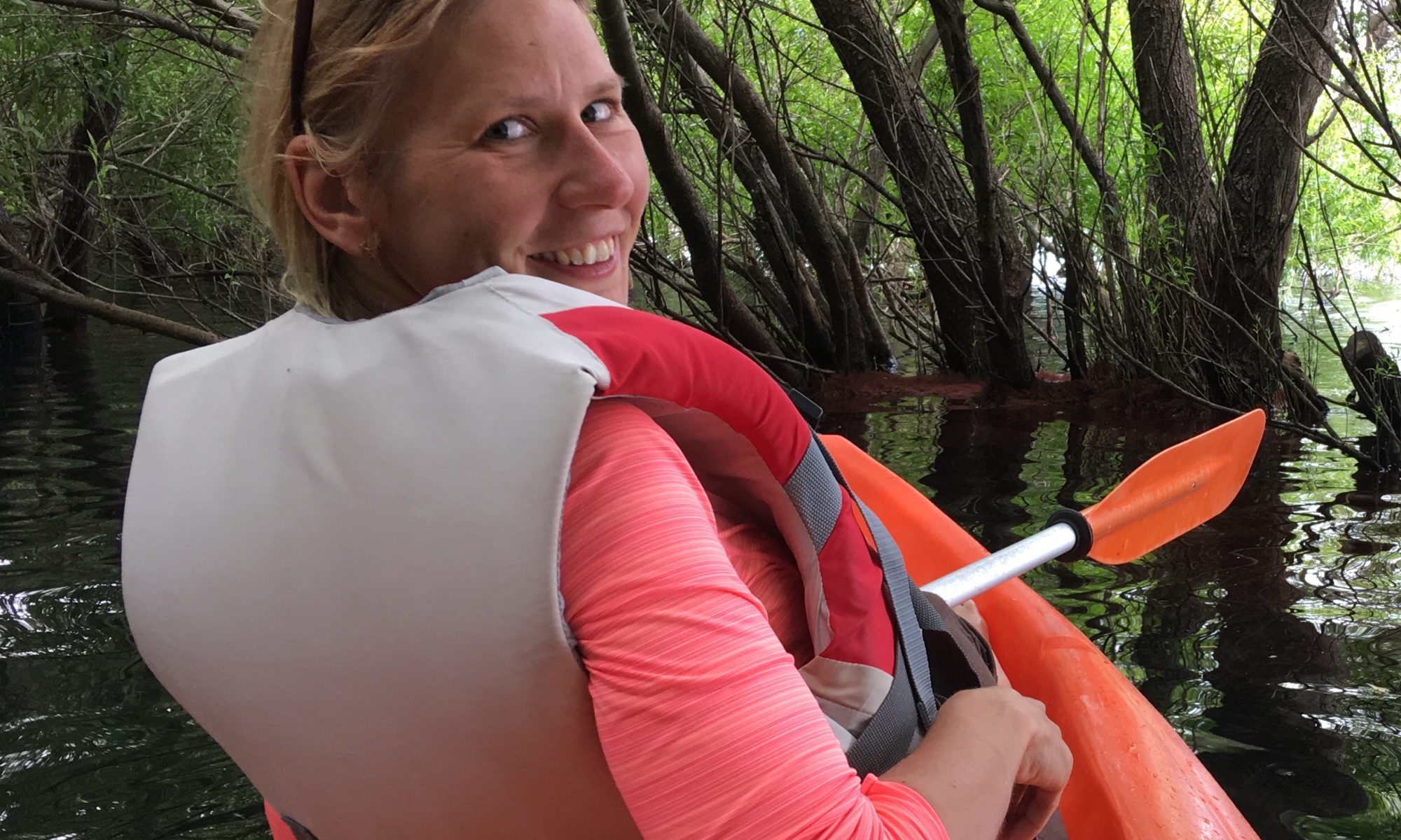 Photo of Żaneta Kaszta floating in a tandem kayak through a wooded lake or pond